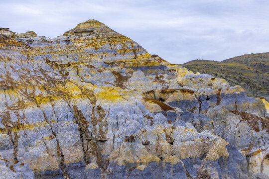 View of layered rock formations with contrasting yellow, blue, and brown hues under a cloudy sky, Shetpe, Mangystau Region, Kazakhstan.