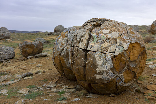 View of spherical rock formations scattered across the arid landscape, weathered and cracked under a cloudy sky, Shetpe, Mangystau Region, Kazakhstan.