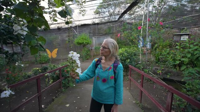 Mature woman takes time to smell flowers inside the butterfly enclosure located on Ometepe Island in Charco Verde Nicaragua.