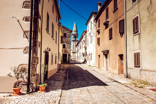 View of sun-drenched stone buildings casting long shadows on the cobblestone street leading to the church tower, Draguc, Istria County, Croatia.