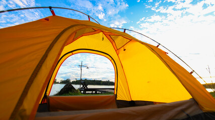 A cozy yellow camping tent pitched on lush green grass by a peaceful lakeside during golden hour. nature travel, and serene outdoor living. Ideal for themes of camping, weekend getaway,