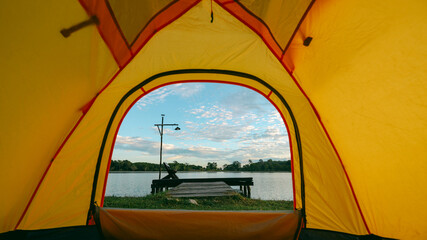 A cozy yellow camping tent pitched on lush green grass by a peaceful lakeside during golden hour. nature travel, and serene outdoor living. Ideal for themes of camping, weekend getaway,