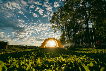 A cozy yellow camping tent pitched on lush green grass by a peaceful lakeside during golden hour. nature travel, and serene outdoor living. Ideal for themes of camping, weekend getaway,