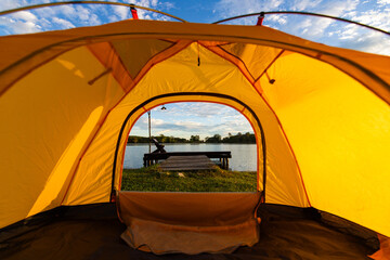 A cozy yellow camping tent pitched on lush green grass by a peaceful lakeside during golden hour. nature travel, and serene outdoor living. Ideal for themes of camping, weekend getaway,