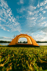 A cozy yellow camping tent pitched on lush green grass by a peaceful lakeside during golden hour. nature travel, and serene outdoor living. Ideal for themes of camping, weekend getaway,