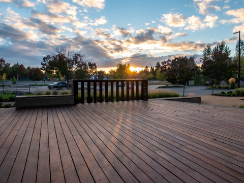 View of the sun's golden glow kissing the wooden deck, casting long shadows as the sky blazes with hues of orange and blue in Apollo Park, Oregon, United States.