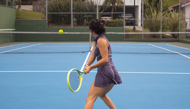Action shot of a young female tennis player executing a two-handed backhand swing during a practice session. Concept of technical learning, resilience, and effort in healthy sports hobbies.