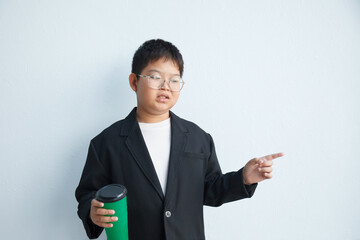 A chubby Asian boy in a suit is holding a coffee cup and pointing his finger against a white background.