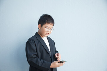 A chubby Asian boy in a suit is using a smartphone against a white background and workspace.
