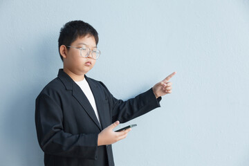 A young businessman in a suit holds a smartphone in his right hand and points to an empty space with his left hand.
