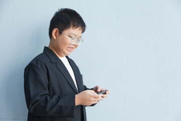 A chubby Asian boy in a suit is using a smartphone against a white background and workspace.