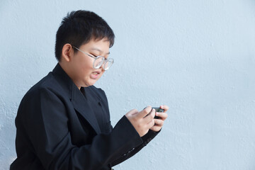A chubby Asian boy in a suit is using a smartphone against a backdrop of a white workspace.