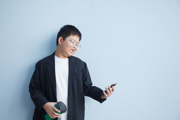 A boy in a suit is holding a coffee cup and smiling while looking at his cell phone.
