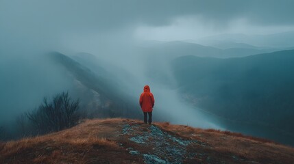 Lone Hiker in Red Jacket Overlooking Misty Mountains.