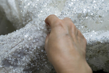 Fototapeta premium The seamstress's hand is sewing beads on a wedding dress stock photo