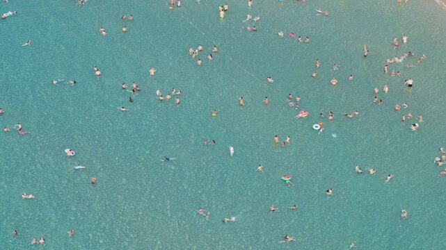 Cefalu, Italy - 12 August 2025: Aerial view of a beach bustling with people enjoying the clear turquoise waters near the shore.