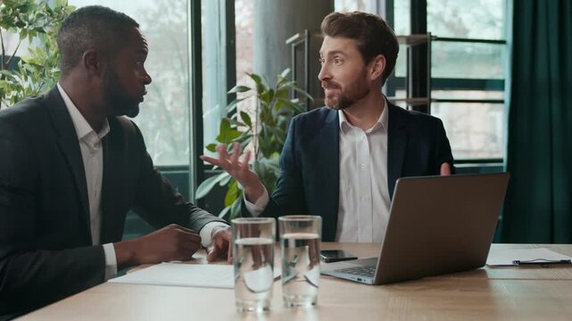 Two business men team in office multiethnic African American businessman sharing good idea Caucasian boss ecxited agree writing notes diversity employers businessmen talking with laptop carefree job