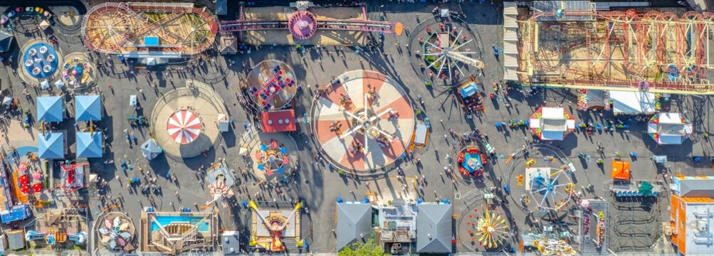 Aerial view of a vibrant Coney Island amusement park, the rides casting long shadows over crowds of people, Brooklyn, New York, United States.