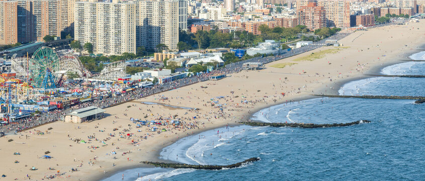 Aerial view of sun-drenched Coney Island beach, where the iconic Ferris wheel and rollercoasters meet the vast ocean, Brooklyn, New York, United States.