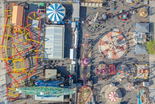 Aerial view of a vibrant tapestry of amusement park rides and bustling crowds, showcasing the iconic roller coaster tracks, Coney Island, Brooklyn, New York, United States.