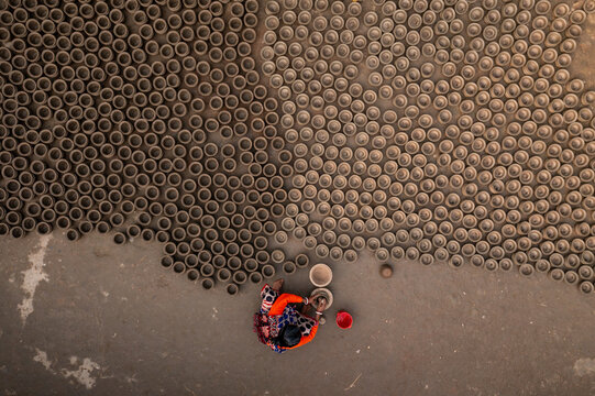 Bogura, Bangladesh - 27 January 2020: Aerial view of a woman amidst hundreds of pottery items, their circular forms creating an intricate pattern against the sandy ground.
