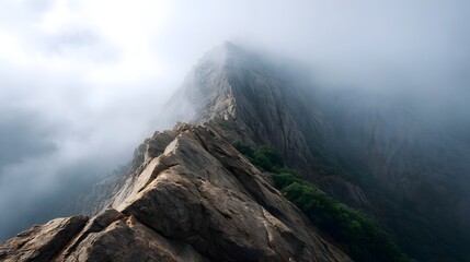 A dramatic mountain ridge emerges from swirling fog showcasing rugged rock formations and steep slopes under a misty sky