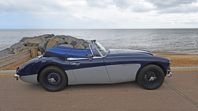 Classic Austin-Healey 3000 MkIII parked on seafront promenade beach and sea in background.
