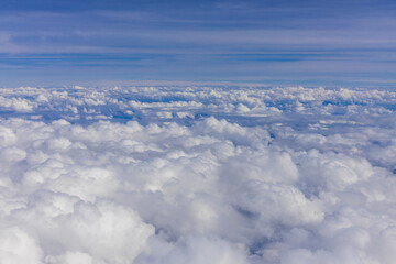 Fototapeta premium Cloud layers in the sky seen from airplane window with wing edge, aerial travel perspective, white cumulus and cirrus formations above landscape, aviation altitude view, weather patterns, daylight fli