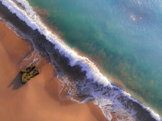 Aerial view of turquoise waves crashing onto the golden sands, their foamy crests contrasting with the dark, mossy rocks and the clear blue sea, Salcombe, England, United Kingdom.