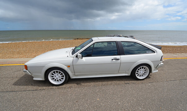 Classic VW Scirocco in  White  parked on seafront beach and sea in background