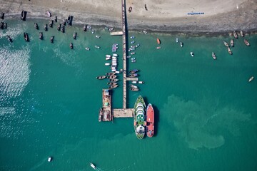 Aerial view of boats clustered near a pier extending into the turquoise sea, their hulls a vibrant contrast to the sandy shore, Cox's Bazar, Chittagong Division, Bangladesh.