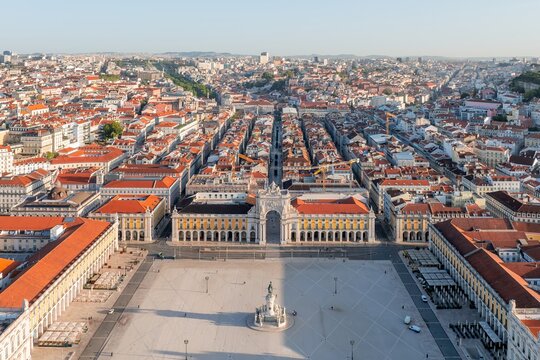 Aerial view of the expansive Pra&Atilde;&sect;a do Com&Atilde;&copy;rcio, its grand archway framing the city's skyline, a vibrant contrast of terracotta roofs against the Tagus River's glimmer, Lisbon, Lisbon, Portugal.