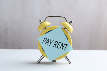 Time to pay rent. Paper note attached to alarm clock on table