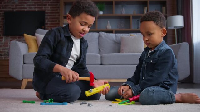 Two ethnic little boys African American kids playing at home joyful play with toys sons siblings children focused with renovation game using repair tools in apartment playful building family indoors