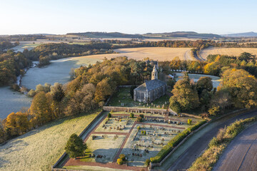 Aerial view of a stone church with a graveyard encased in a stone wall, surrounded by fields and trees in autumn colors, Cupar, Scotland, United Kingdom.