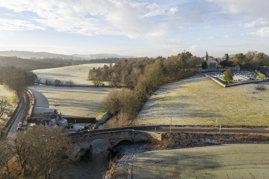 Aerial view of a tranquil landscape where frosty fields meet the ancient Cupar Old Parish Church, its spire piercing the soft morning light, Cupar, Scotland, United Kingdom.