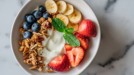 A bowl filled with yogurt topped with blueberries strawberries banana slices and granola sits on a stone surface. This is prepared for breakfast in the morning.