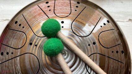 Steel tongue drum close up with two mallets featuring green felt heads on a wooden background. Professional musical instrument for meditation and relaxation © AndreyZayats