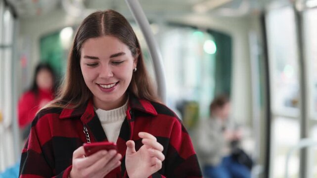 Girl with long hair holds on to a curse during a trip in a tram, she looks at a map of the city on an application on her phone. European woman using public transport