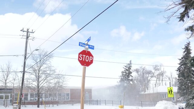 Ice and snow blowing through a residential neighborhood in Mississauga, Ontario, Canada. Stop sign and Vista Blvd. street signs.
