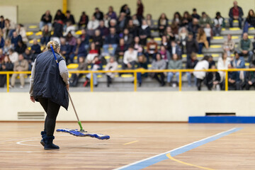 Person cleaning gymnasium court floor during event