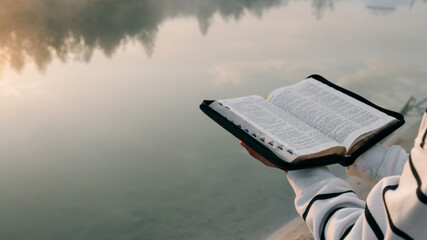 Person reading a Bible by a misty lake at sunrise, seeking spiritual connection