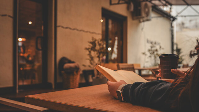 Person reading a book and holding a coffee cup at an outdoor cafe table