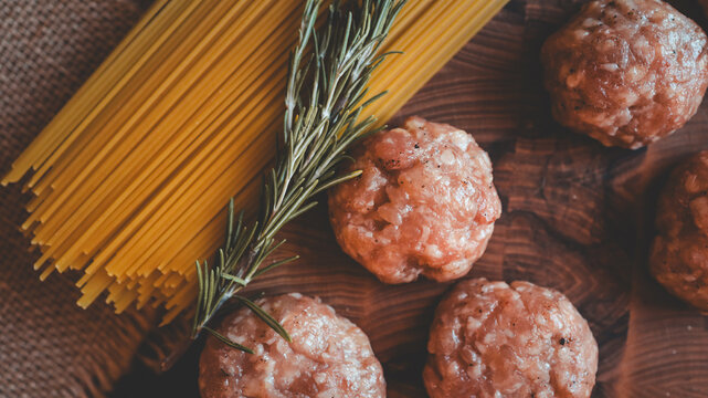 Raw spaghetti and meatballs with rosemary on a wooden board, ready for cooking
