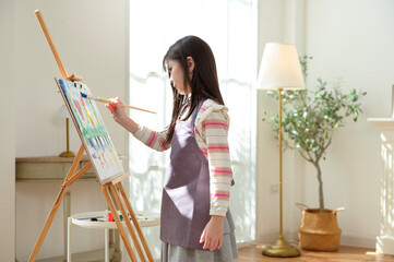 Child Creates Art While Standing at an Easel in a Bright Room During Daytime