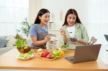 Friends Preparing a Healthy Meal Together in a Bright Kitchen While Using a Laptop for Recipes