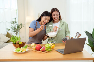 Friends Preparing a Healthy Meal Together in a Bright Kitchen While Using a Laptop for Recipes