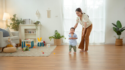 Boy Takes His First Steps at Home While Holding His Mother's Hand in a Warm Living Room Setting
