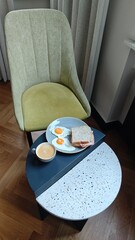 Plate with fried egg ham cheese sandwich and coffee on a small table in a cozy cafe setting. The image represents classic breakfast routine comfort food and relaxed morning lifestyle