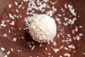 Single coconut cream truffle with white coco flakes in wooden bowl. 